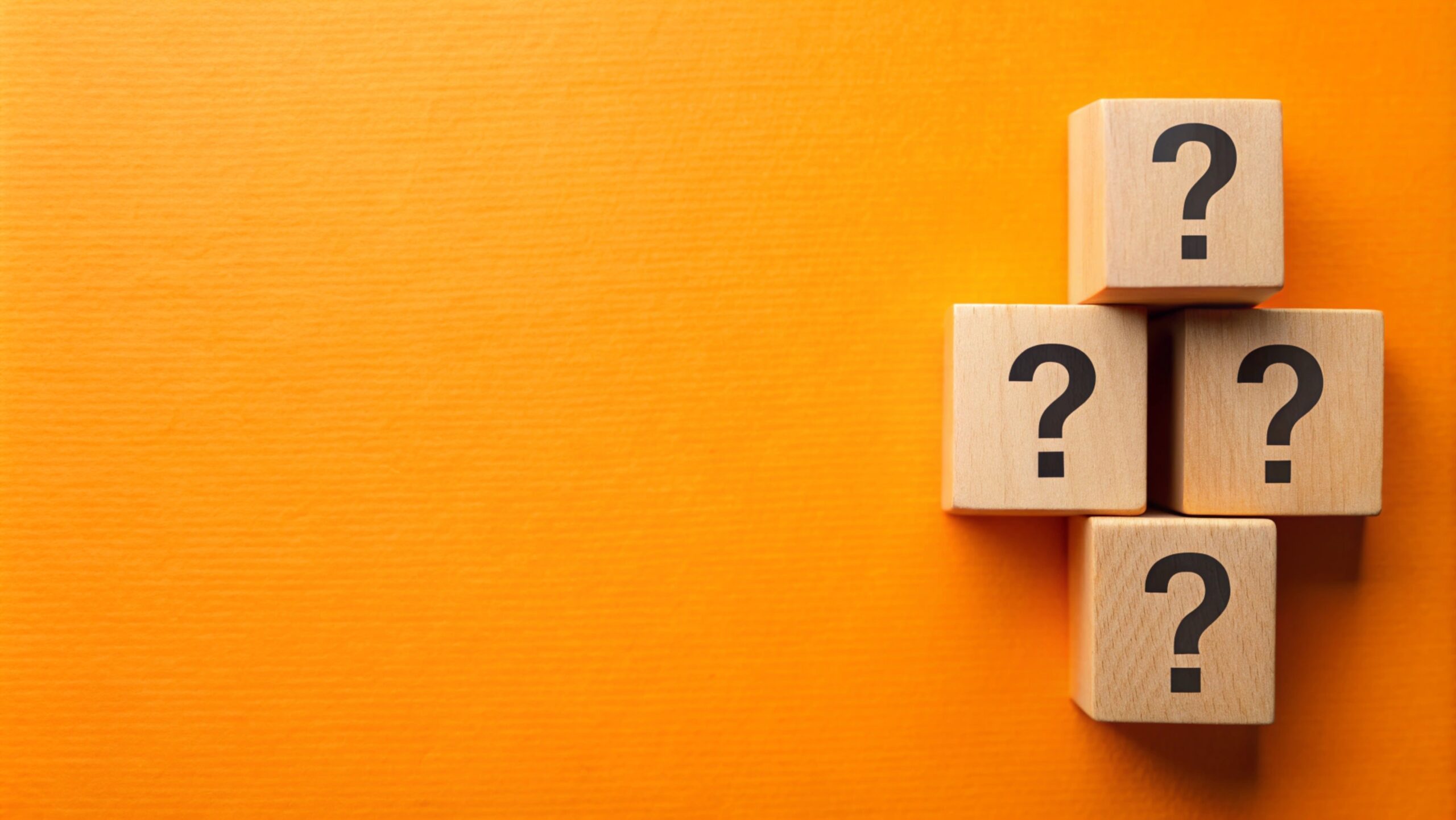 Stock photo of a stack of blocks displaying question marks, set against an orange background